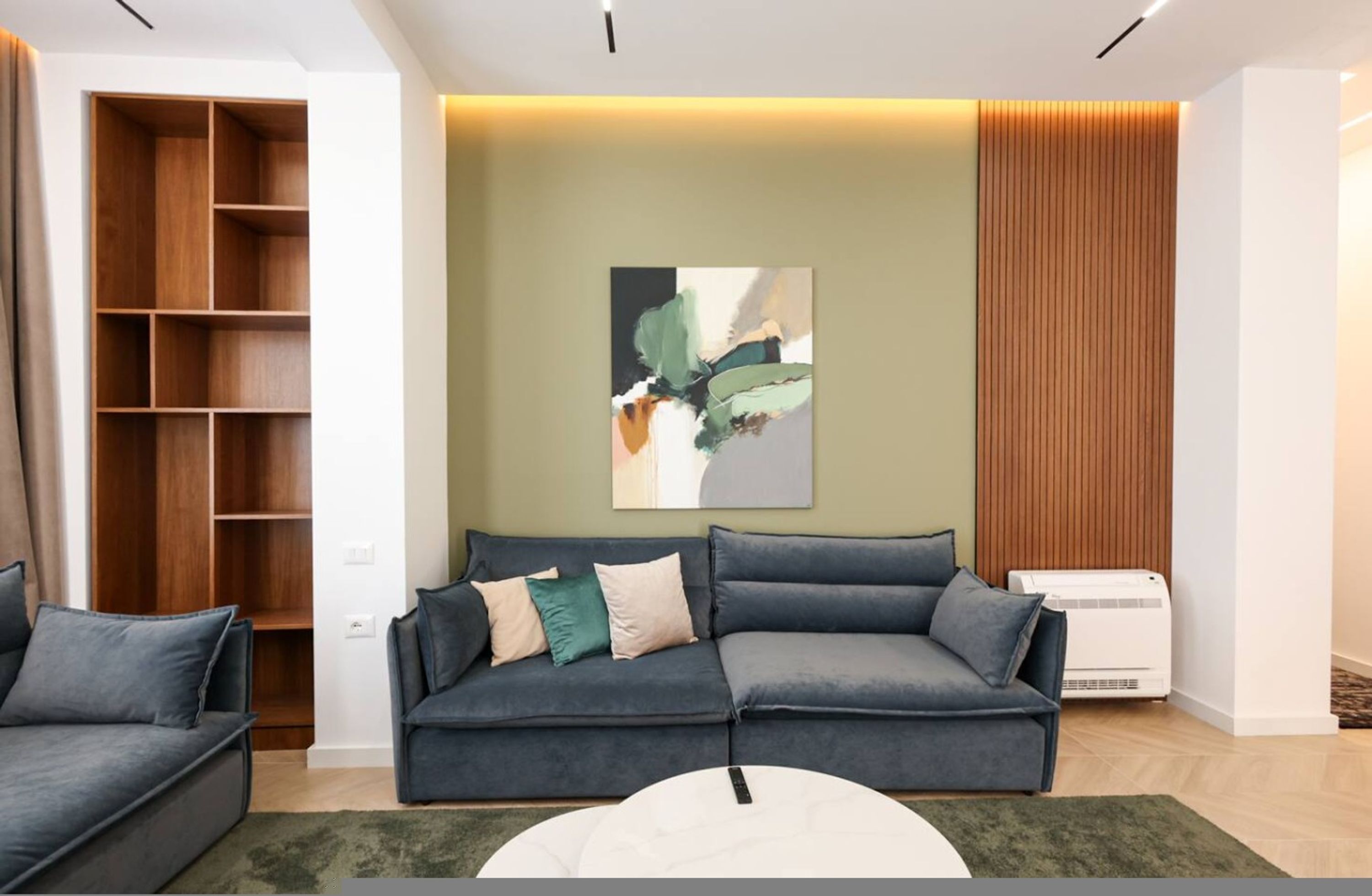 Een moderne woonkamer met een grijze bank, een witte salontafel en een houten wandplank.