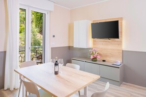 Une pièce comprenant une table à manger, des chaises, un téléviseur fixé à un mur en bois, un petit meuble et une vue sur l’extérieur, visible à travers une porte vitrée.