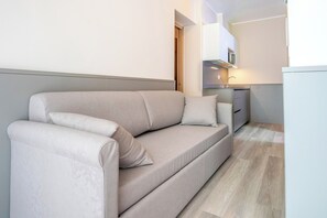 Un salon moderne avec un canapé, un coin cuisine équipé d’un évier et de placards, et un plancher en bois.