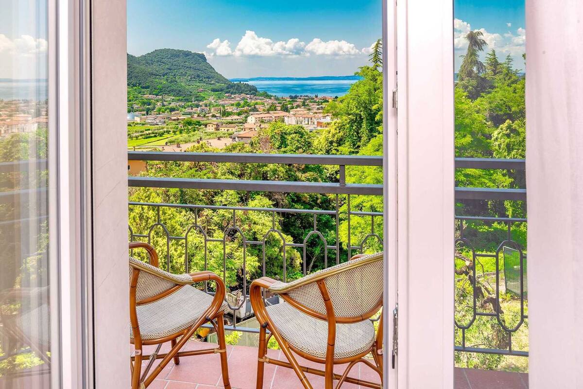 A balcony with wicker chairs and a view of a coastal town.