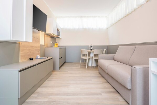 Une cuisine compacte avec un coin repas, un canapé et un téléviseur fixé au mur.