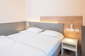 A neatly made double bed with white linens, a bedside table with a lamp, and a wall-mounted light fixture. - Residence Panorama (Suzzara)