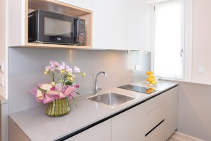 Une cuisine moderne équipée d’un four à micro-ondes encastré, d’un évier en acier inoxydable et agrémentée d’un vase de fleurs.
