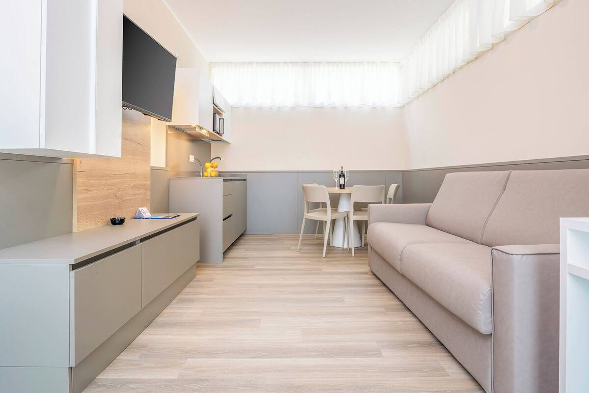 A compact kitchen with a dining area, a sofa, and a TV mounted on the wall.