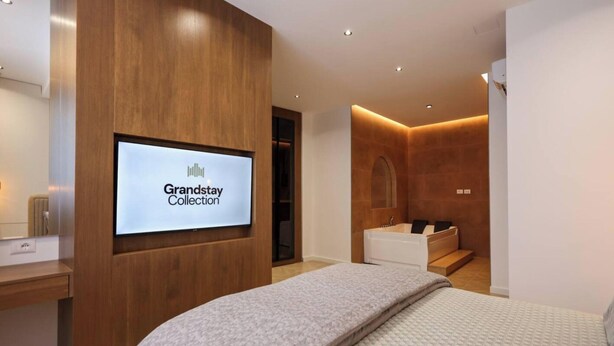 Camera d'albergo moderna con un letto, un angolo trucco e una zona doccia, con il cartello Grandstay Collection.