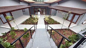 Un edificio moderno con una escalera central, dos zonas ajardinadas con plantas y una bicicleta estacionada afuera.