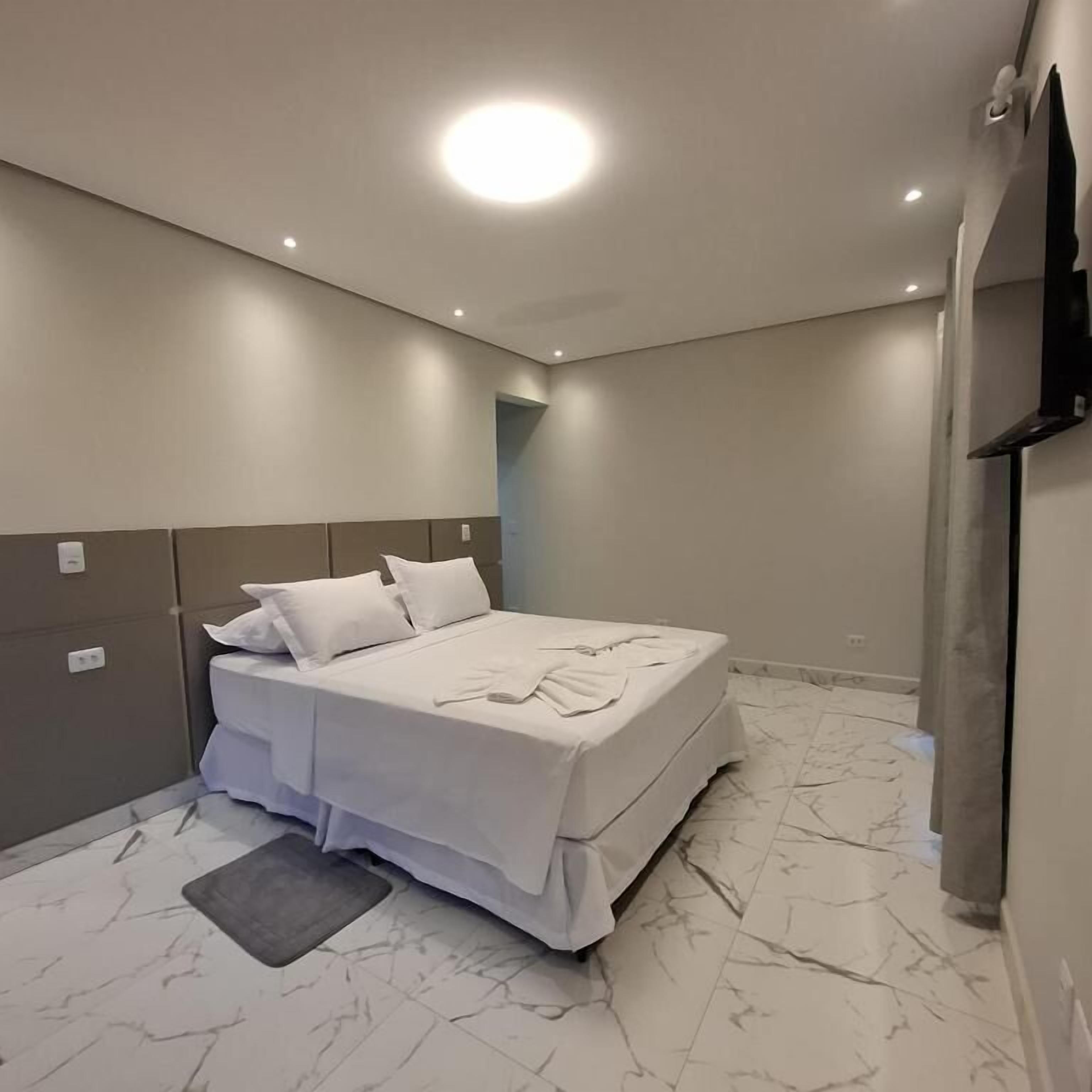 A modern bedroom with a bed, a flat-screen TV, and a marble floor.