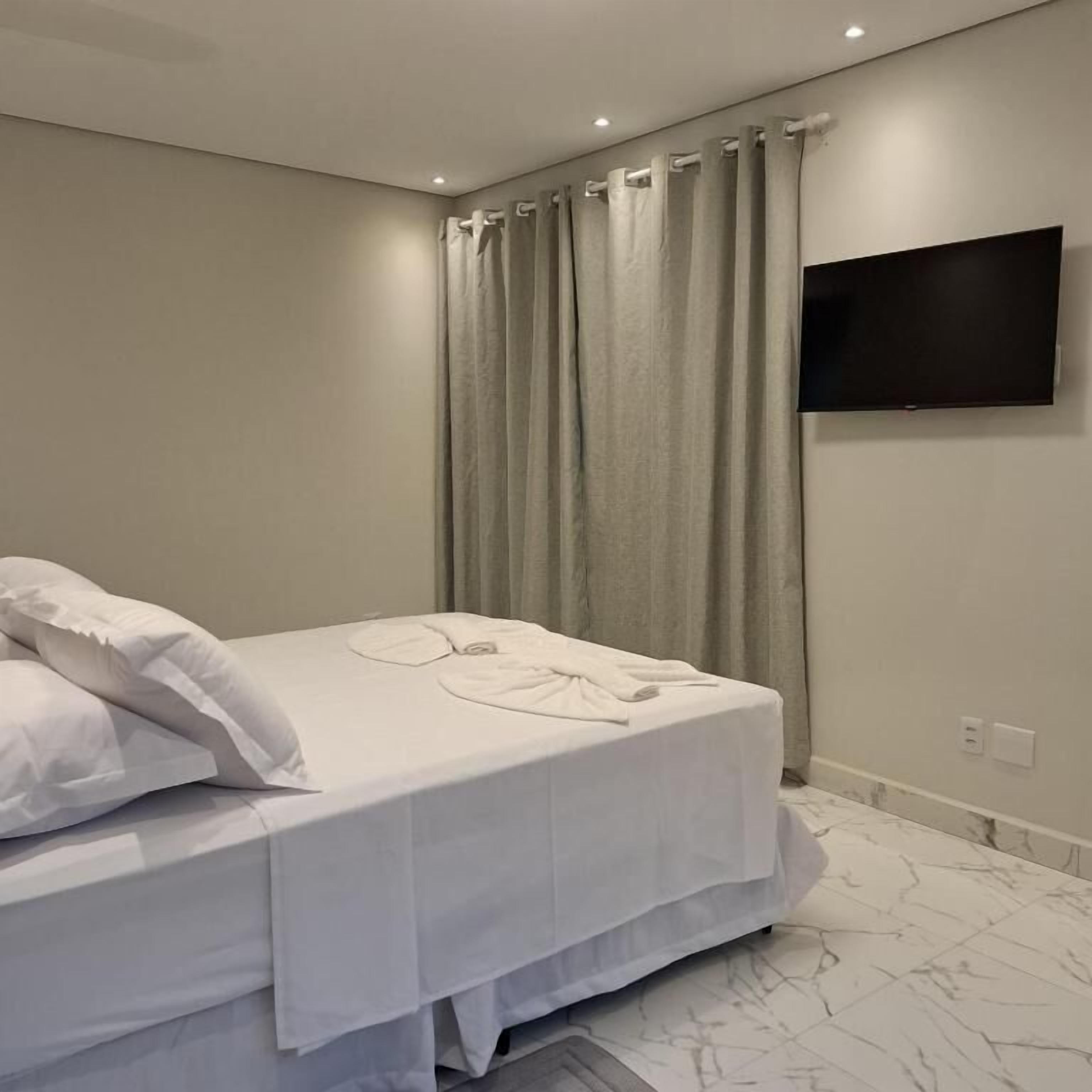 A bedroom with a bed, curtains, a flat-screen TV, and a marble floor.