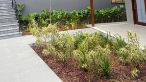 Un edificio de dos pisos con balcón, escalera y jardín con diversas plantas.