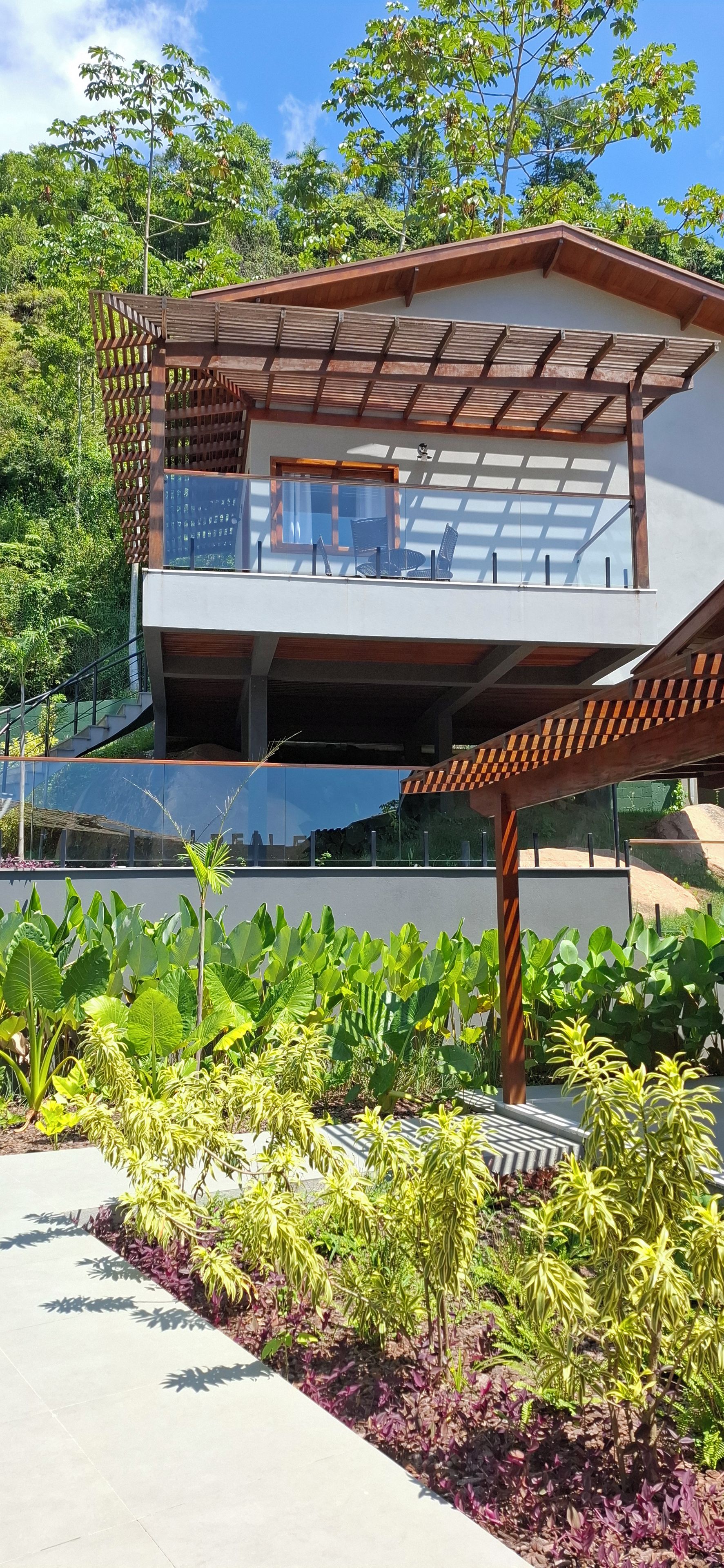 Un edificio de dos pisos con un balcón, rodeado de exuberante vegetación y un cielo despejado.