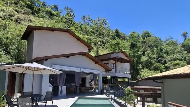 Una piscina con un porche cubierto, rodeada de abundante vegetación.