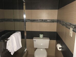 A bathroom with a glass shower enclosure, a toilet, and a towel rack. - Crimson Hotel (Manhattan Beach)