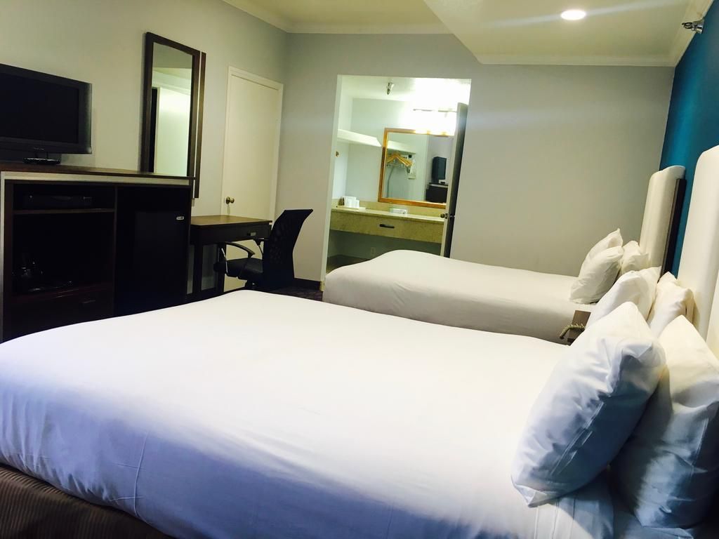 A hotel room with two beds, a desk, a television, and a mirror.