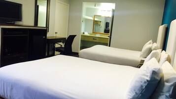 A hotel room with two beds, a desk, a television, and a mirror.