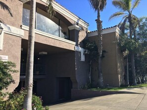 A two-story building with a garage, palm trees, and a clear sky. - Crimson Hotel (Manhattan Beach)