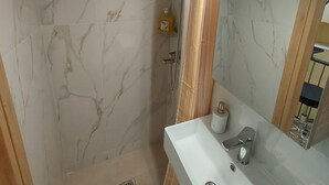 Een badkamer met een douche, wastafel en spiegel.