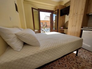 Ein Bett mit gesteppter Matratze, ein an einer Holzwand befestigter Fernseher und ein Küchenbereich mit Kühlschrank.