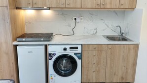 Een kleine keuken met houten kastjes, een ingebouwde wasmachine en een aanrecht met een spoelbak.