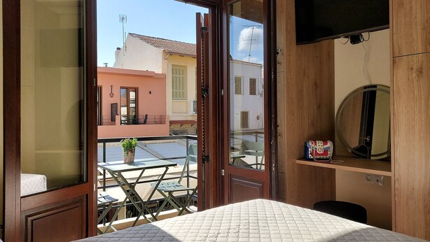 Een kamer met een bed, een aan de muur bevestigde televisie, een kleine tafel met een plant, en een balkon met een tafel en stoelen.