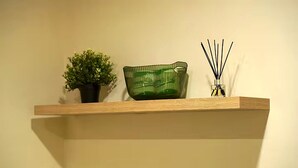 En hylde med en potteplante, en grøn glas skål og en diffuser med rør