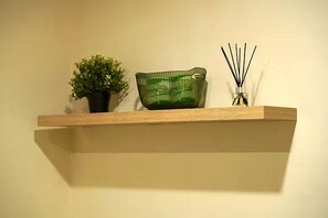 Ein Regal mit einer Blumentopf-Pflanze, einer grünen Glasschale und einem Reed-Diffuser.