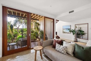 A living room with a sofa, a coffee table, and a sliding glass door leading to a garden.
