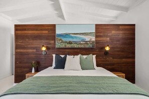 A bedroom with a wooden headboard, a bed with a green blanket, two bedside lamps, and a framed picture on the wall.