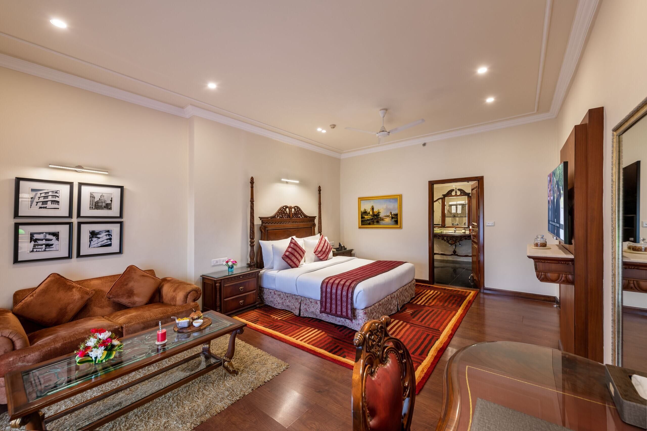 Une chambre d’hôtel avec un lit, un canapé, une table basse, une télévision et des tableaux encadrés au mur.