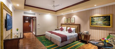 A hotel room with a large bed, a dining table, a sofa, and a ceiling fan.