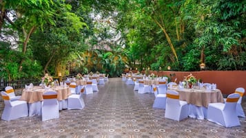 Een openluchtrestaurant met ronde tafels en witte stoelen, omringd door weelderige begroeiing.
