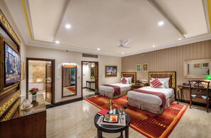 A hotel room with two beds, a desk, a chair, a TV, and a dining area with a table set for two. - Mayfair Lagoon Bhubaneswar (Bhubaneshwar)