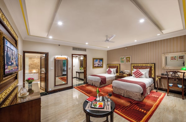 A hotel room with two beds, a desk, a chair, a TV, and a dining area with a table set for two. - Mayfair Lagoon Bhubaneswar (Bhubaneshwar)