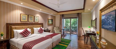 A hotel room with a large bed, a desk, a chair, a balcony with a view, and framed pictures on the wall.