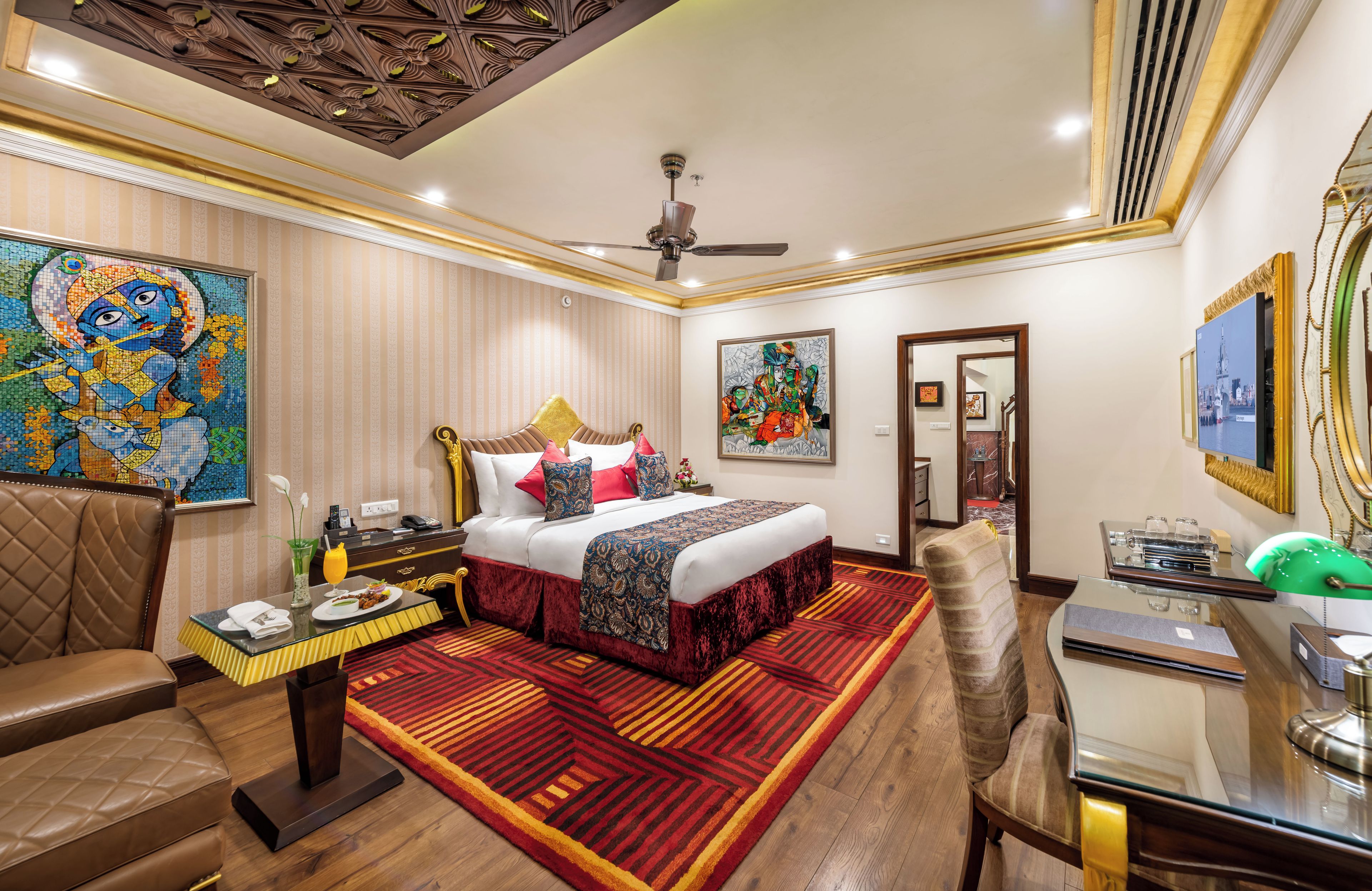 A hotel room with a bed, a desk, a chair, a dining table, and artwork on the walls.