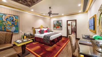 A hotel room with a bed, a desk, a chair, a dining table, and artwork on the walls.