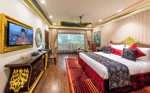 A hotel room with a large bed, a desk with a television, a chair, a window with curtains, and a ceiling fan. - Mayfair Lagoon Bhubaneswar (Bhubaneshwar)