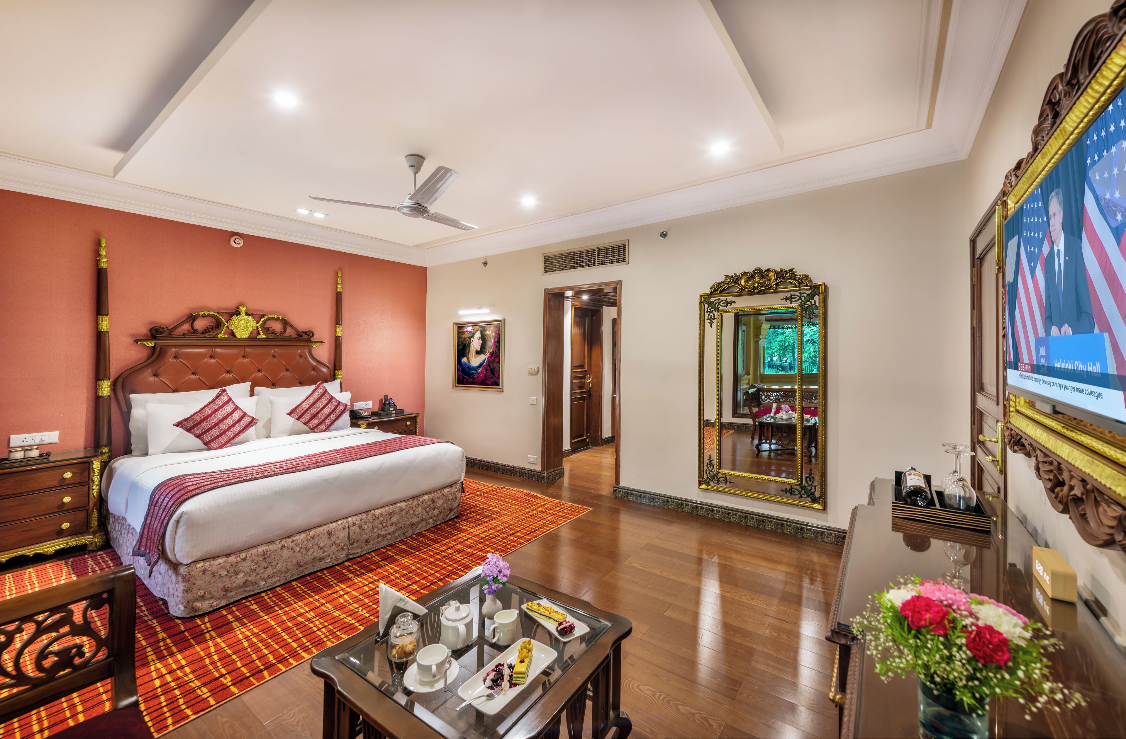 A hotel room with a large bed, a ceiling fan, a television, a mirror, and a dining table with a tray of food.