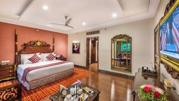 A hotel room with a large bed, a ceiling fan, a television, a mirror, and a dining table with a tray of food.