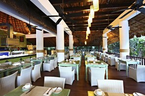 Un restaurant doté d'une terrasse, de chaises en osier blanches, de tables dressées et d'un toit de chaume.