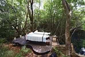 Un coin de forêt isolé avec une terrasse en bois, deux lits et une petite table sur laquelle se trouve un bol.