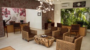 A reception area with wicker furniture, a stone coffee table, and a large floral painting on the wall. - Sandos Caracol Eco Resort - Select Club - All Incl (Playa del Carmen)