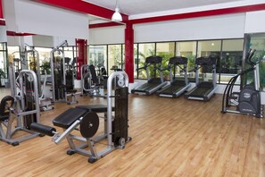 Une salle de sport équipée de divers appareils d’exercice, notamment des tapis de course et des appareils de musculation, avec de grandes fenêtres et un plancher en bois.