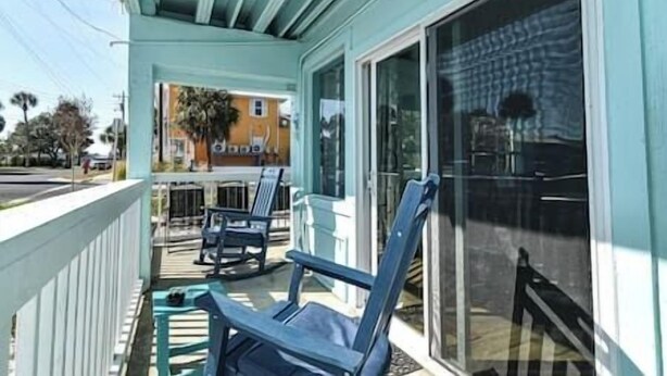 A covered porch with two chairs and a table, a sliding glass door, and a view of a building with a palm tree. - Cedar Key Turtle 132 (Cedar Key)