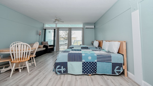 A bedroom with a large bed, a desk, and a chair. There is a window with a view of the outside. - Little Blue Anchor Condo 124 (Cedar Key)