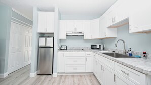 A modern kitchen with white cabinets, stainless steel appliances, and a marble countertop. - Little Blue Anchor Condo 124 (Cedar Key)