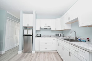 A modern kitchen with white cabinets, stainless steel appliances, and a marble countertop. - Little Blue Anchor Condo 124 (Cedar Key)