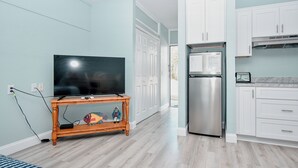 A modern kitchen with white cabinets, a stainless steel refrigerator, and a wooden console table with a television. - Little Blue Anchor Condo 124 (Cedar Key)