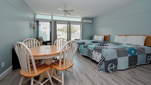 A room with a dining table and chairs, a bed with a patterned bedspread, and a ceiling fan. - Little Blue Anchor Condo 124 (Cedar Key)