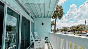 A covered porch with two rocking chairs, a sliding glass door, and a white railing. - Little Blue Anchor Condo 124 (Cedar Key)