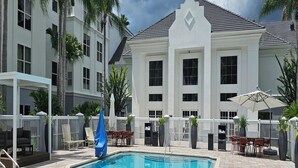 A swimming pool with a white fence, palm trees, and a building with large windows. - Revival Scottsdale Studios (Orlando)